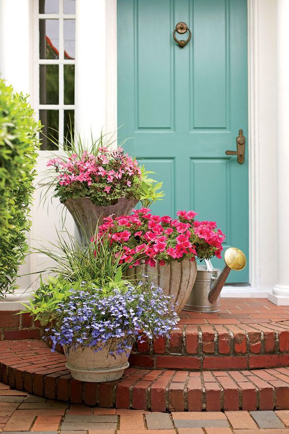 a bright spring porch with bold flowers in containers and a blue door that adds interest and eye-catchiness to the space