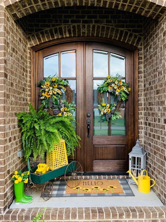 a bright spring porch with layered rugs, a small cart with lanterns, potted greenery and green rubber boots with blooms