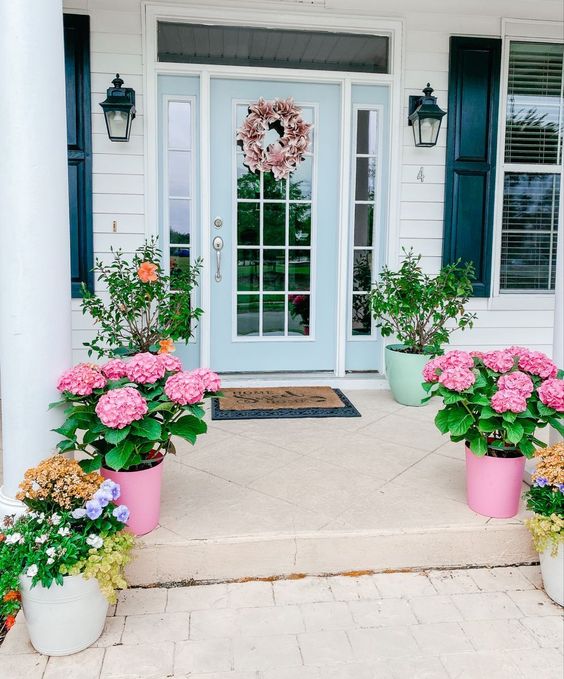 a bright spring porch with potted bright blooms and greenery, rugs and a pink wreath is amazing