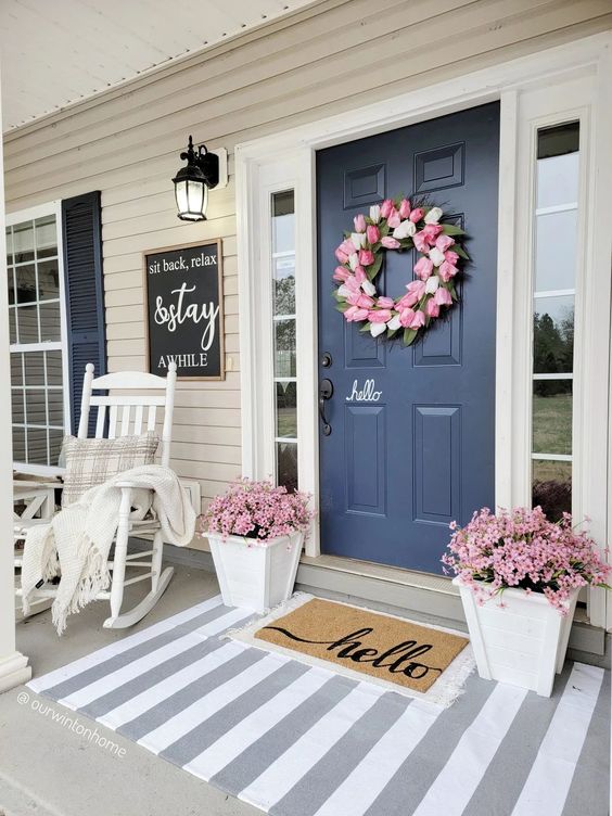 a classic spring porch with potted pink blooms, a pink tulip wreath and a white rocker chair with a blanket