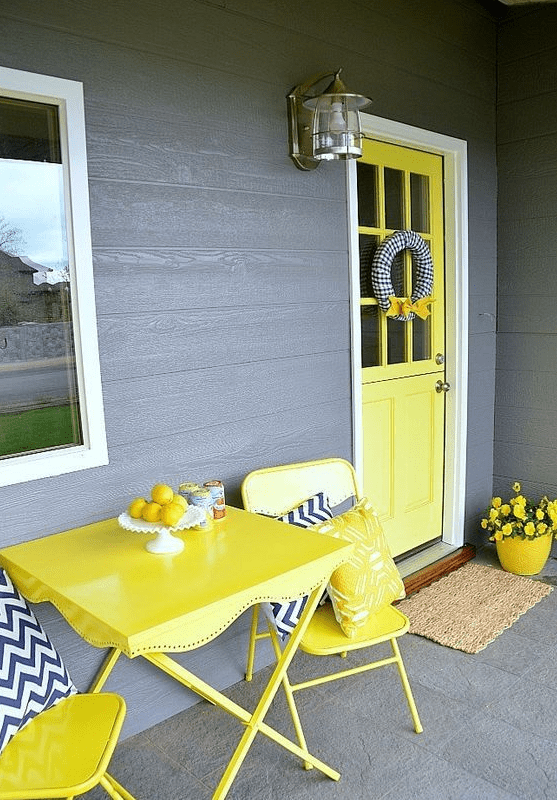 a colorful spring porch with yellow furniture, door and a pot plus blooms and chevron pillows