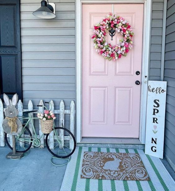 a cute porch with a blush door and a pink tulip wreath, a bike with a basket of blooms and a bunny sign and layered rugs