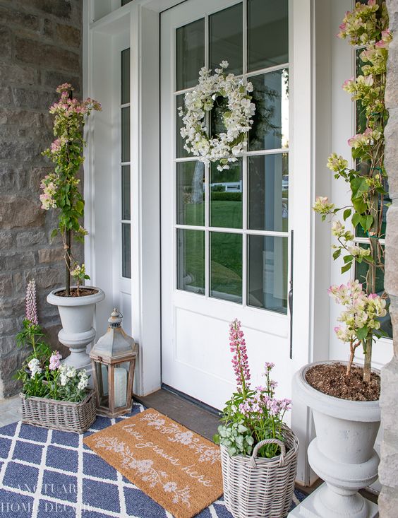a fresh spring porch styled with potted blooms and greenery, baskets with flowers and lanterns plus layered rugs