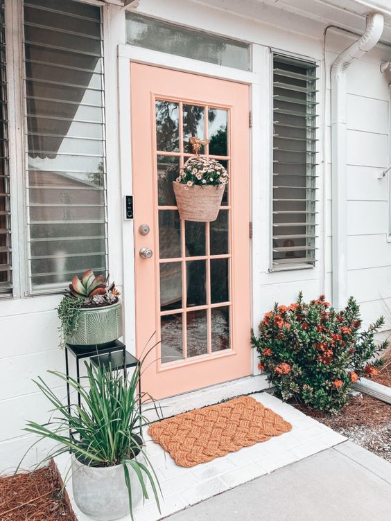 a pretty spring porch with a pink door, blooms and greenery and a basket with flowers instead of a wreath is amazing