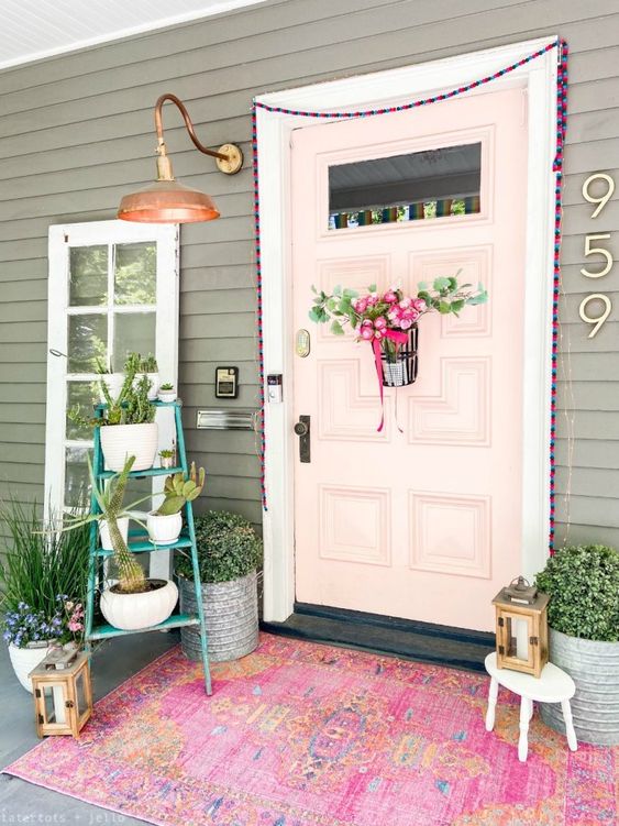 a pretty spring to summer porch with pink blooms, potted greenery and a bright pink rug and some garlands