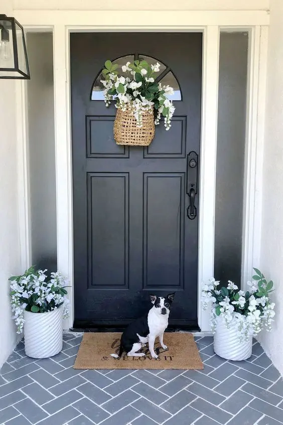 a simple and cool spring porch with a rug, potted white blooms and a basket and a lovely pup