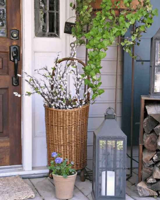 chic spring porch decor with a basket with pussy willow, a candle lantern and some greenery and blooms to embrace the season