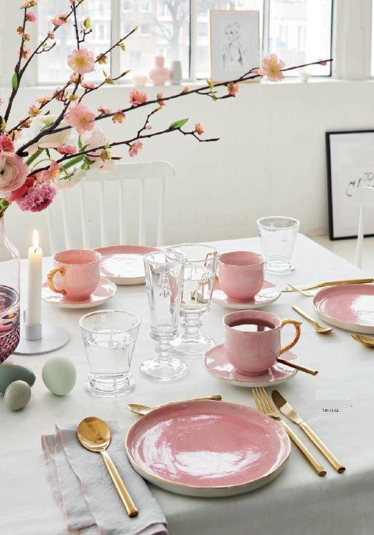 a chic modern Easter tablescape with pink plates and cups, fresh pink blooms, pastel eggs, candles and gold cutlery