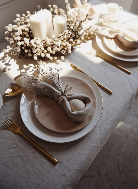 a chic neutral Easter tablescape with a willow and candle centerpiece, pink and white plates, bunny-shaped napkins with eggs and gold cutlery