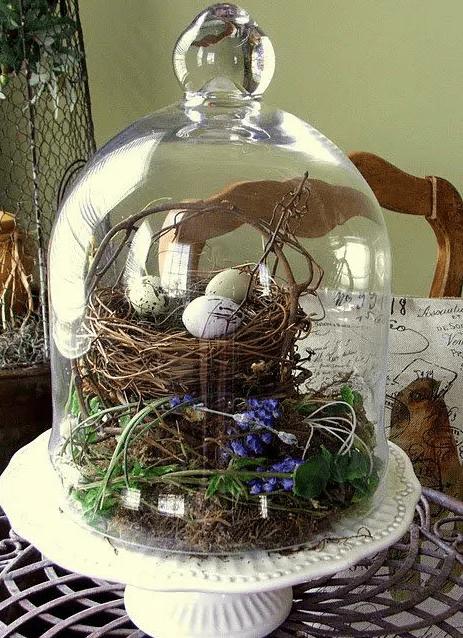 a cloche with a nest and fake eggs, some greenery, blooms and vines is a cool rustic decoration for Easter