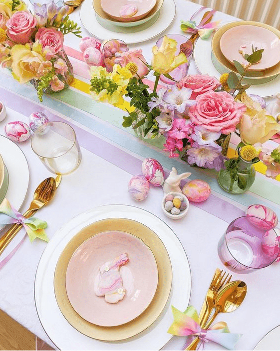 a colorful Easter tablescape with bright blooms, pastel plates, colorful glasses, gold cutlery and bright marble eggs