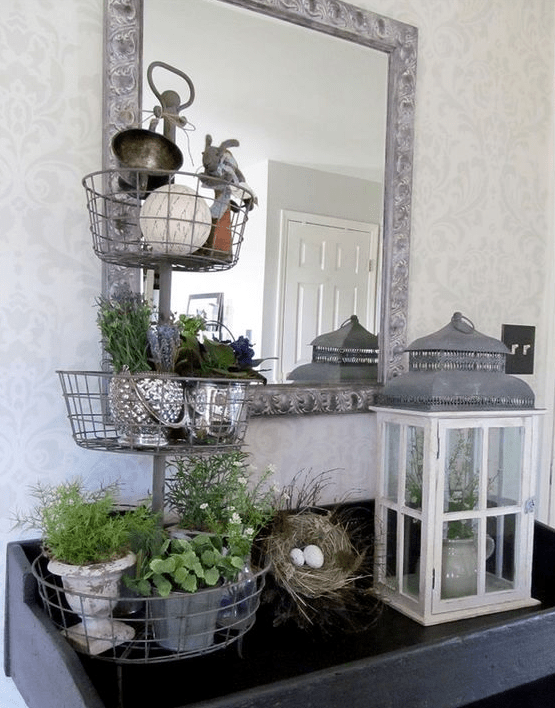 a console with a faux nest with eggs, a lantern and a stand with potted greenery and flowers