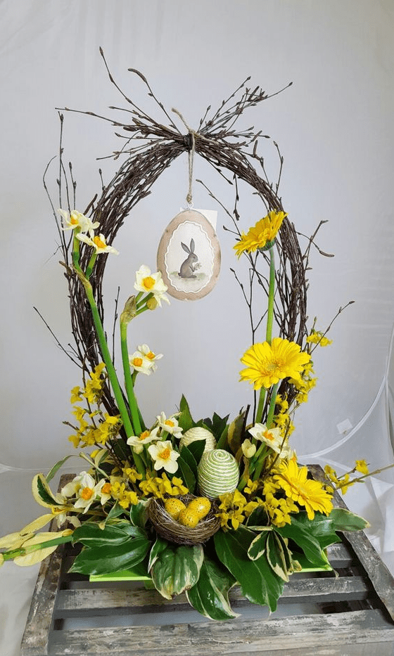 a cute Easter flower arrangement with a basket of vine, yellow blooms and foliage, some eggs and a nest with yellow eggs