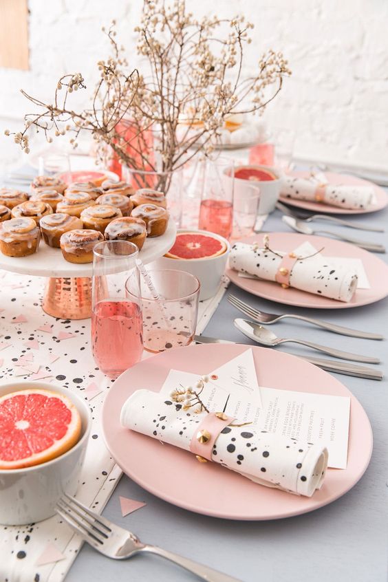a cute Easter tablescape with a speckle runner and napkins, pink plates and napkin rings, dried blooms and bowls with fruits