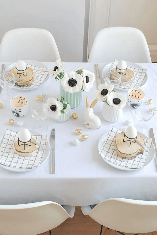 a cute and simple Easter tablescape with printed napkins, wood slices with eggs on stands, white blooms, bunnies and faux mini eggs