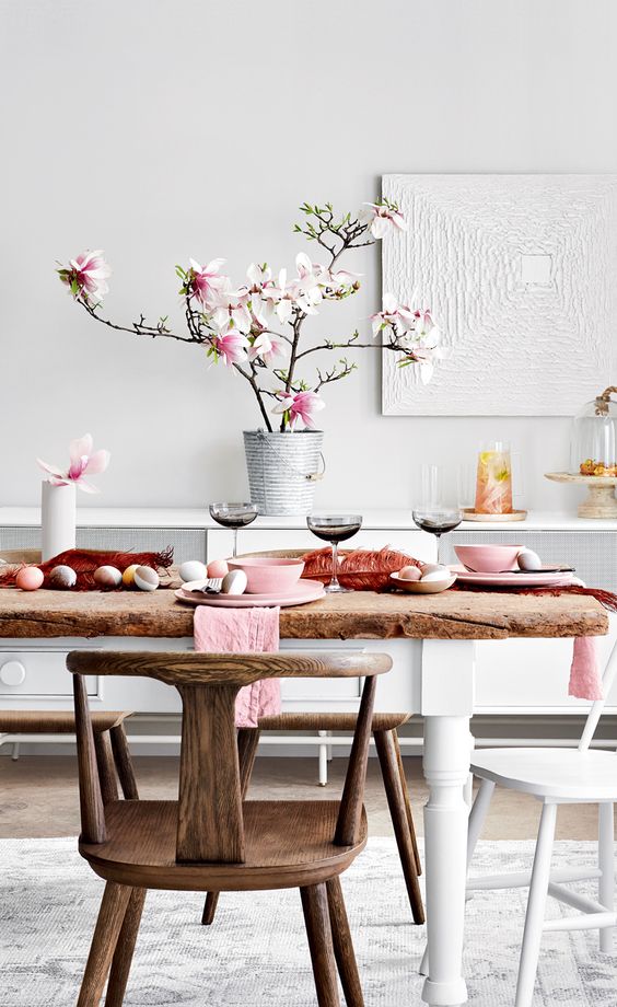 a lovely modern Easter tablescape with a rough wood table, pastel eggs, cherry blossom, pink porcelain and pink napkins
