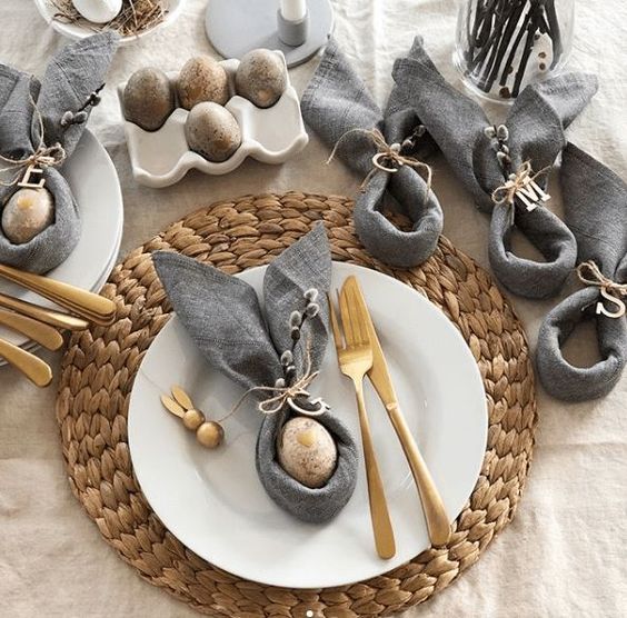 a modern Easter place setting with a wovne placemat, white porcelain, some eggs, grey napkins and gold cutlery