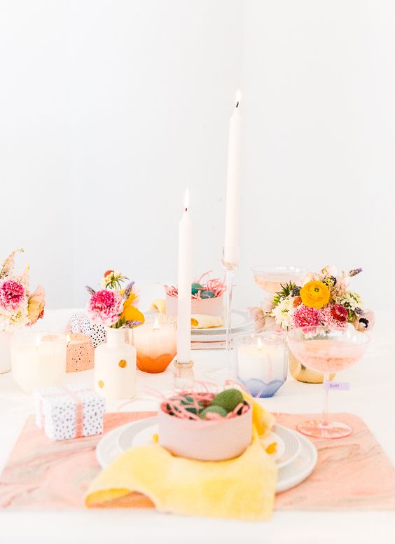 a modern colorful Easter tablescape with peachy placemats, pastel porcelain, bright blooms, candles and speckled candleholders
