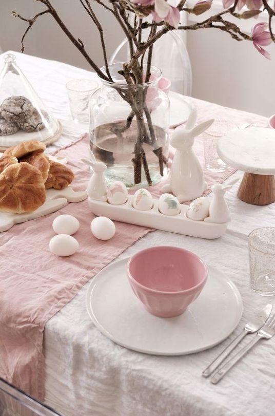 a pastel and neutral modern Easter tablescape with neutral and pink linens, white and pink porcelain, an egg stand with eggs and bunnies and cherry blossom