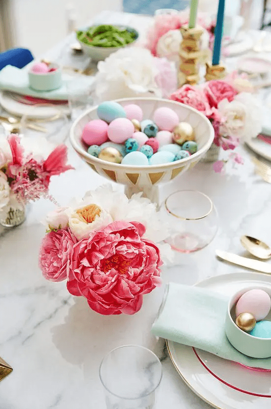 a pretty bright Easter table setting with bold blooms, colorful eggs in a bowl, mint napkins and pastel eggs in a cup