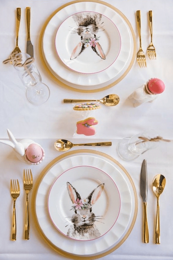 A pretty modern Easter tablescape with bunny printed plates, gold rimmed placemats, gold cutlery and bunny egg holders
