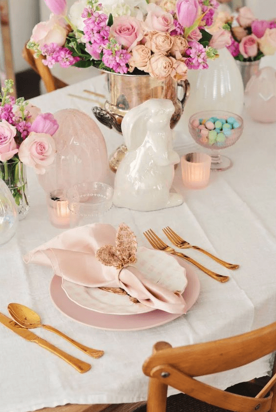 a refined blush and pink Easter table setting with blush and pink blooms, egg and bunny figurines, blush porcelain and gold cutlery