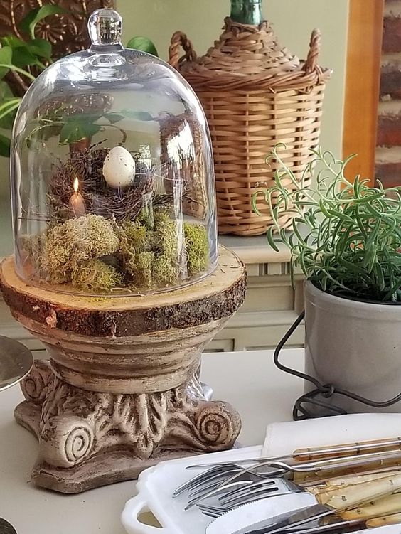 a spring terrarium on a vintage stand, with moss, a faux nest, an egg and a candle is a creative and cool idea