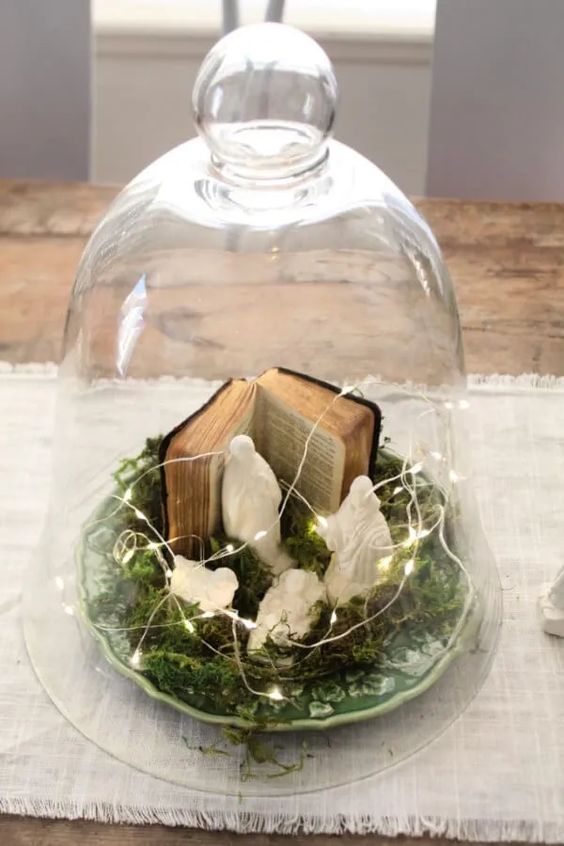 an Easter centerpiece of a cloche with moss, birds, lights and a small book is a cool and catchy decoration to make
