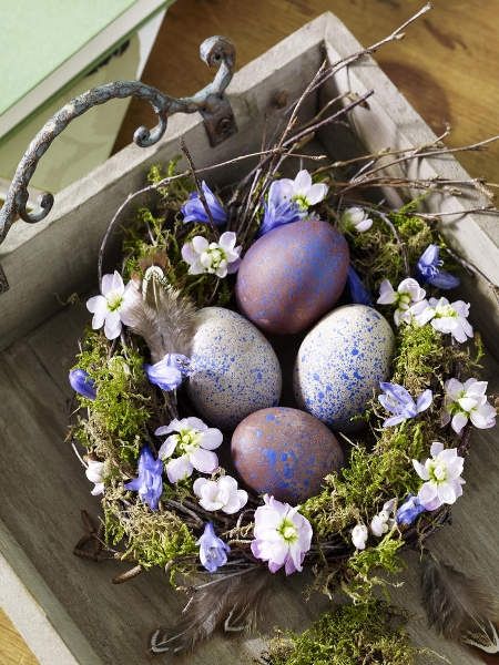 an Easter decoration of a moss nest with bright blooms and blue and purpel speckled eggs is a pretty centerpiece