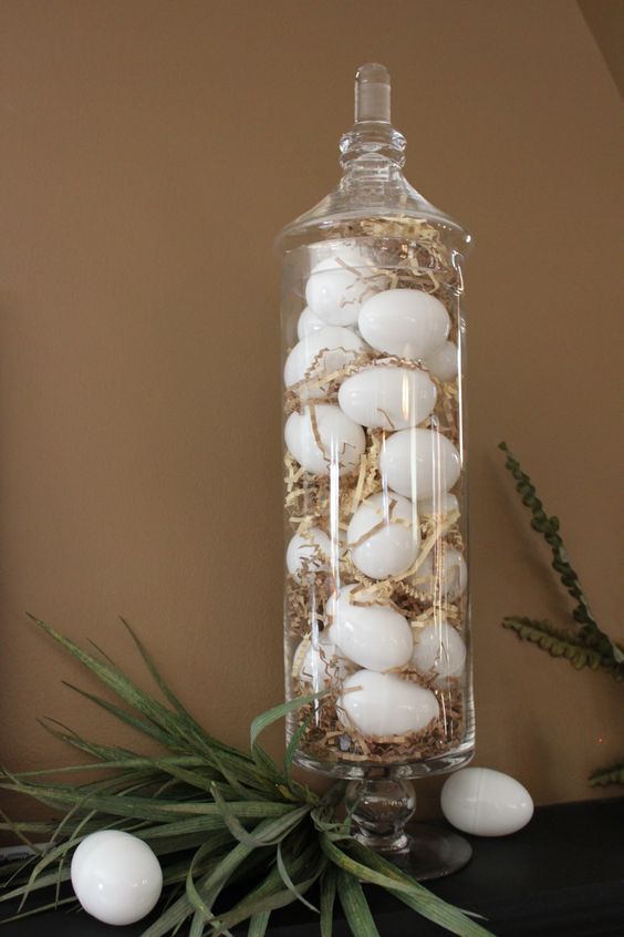 an apothecary jar filled with straw and white eggs