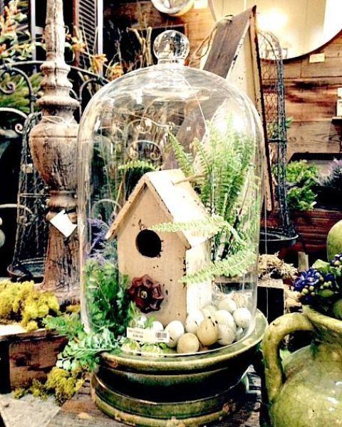 a cloche with a bird house, faux eggs, fern and greenery