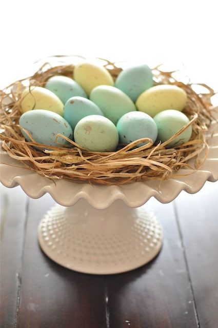 a cake stand with straw and pastel eggs can double as a centerpiece