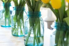 10 blue mason jars with fresh yellow tulips along the table
