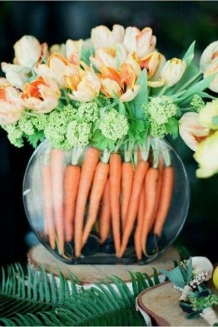 a glass bowl with carrots and orange tulips on top
