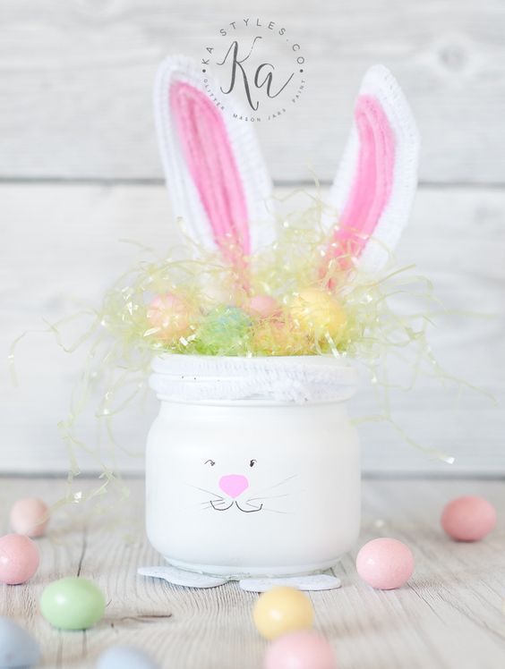 a white mason jar turned into a bunny with ears and pompom eggs