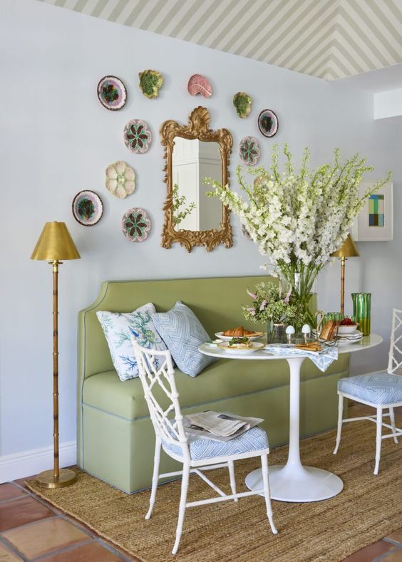 a lovely dining space with a green banquette seating, a table and vintage chairs, a plate wall and a mirror with a gold frame