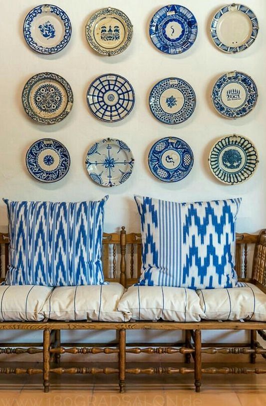 a stained bench with pillows and cushions and a chinoiserie plate wall for an accent are a cool combo for a vintage coastal space