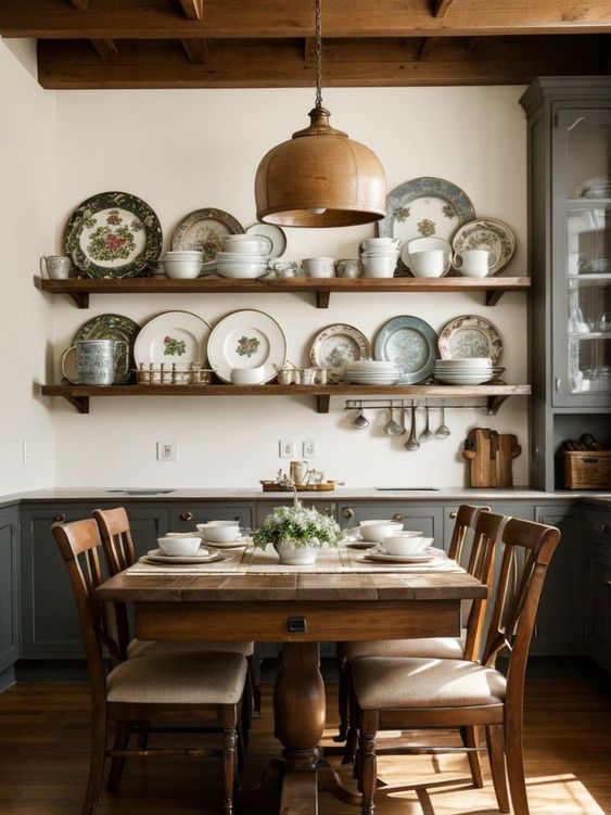 a vintage dining room with grey cabinetry, a stained table and chairs, a stained pendant lamp, open shelves with vintage plates that add chic to the space