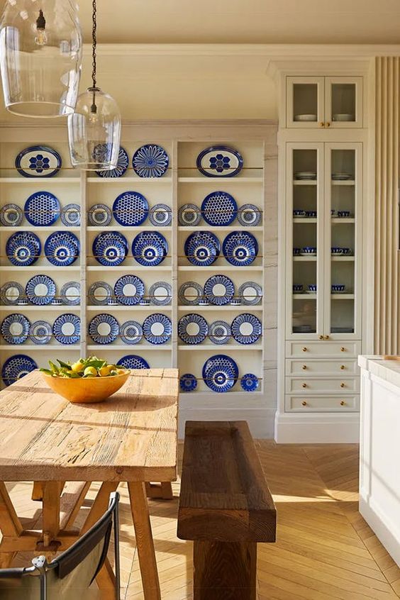 a white farmhouse dining room with a chinoiserie plate wall, stained tables and benches plus pendant lamps is amazing