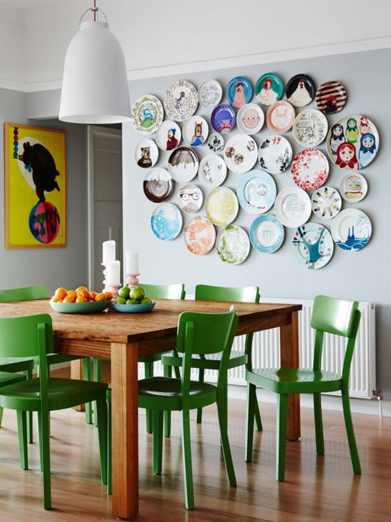 an eclectic dining room with a stained table and green chairs, a plate wall with colorful plates and a poaste plus a pendant lamp is amazing