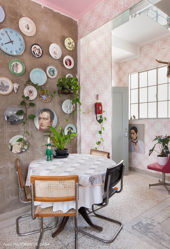 an eclectic dining room with various wallpaper, a dining table and cane chairs, an eclectic gallery wall and some greenery