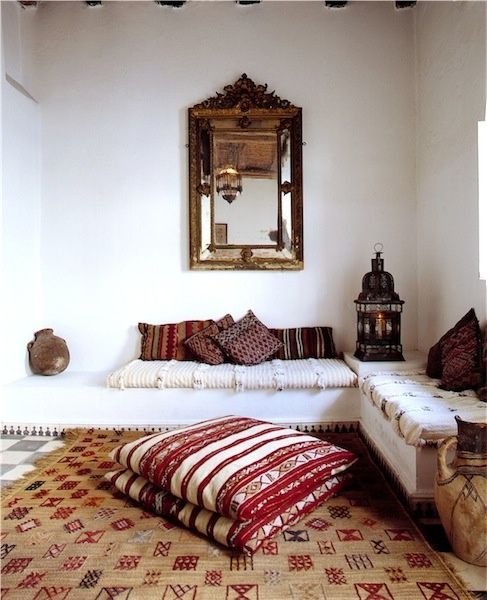 a Moroccan space with printed pillows and a rug and a large refined mirror