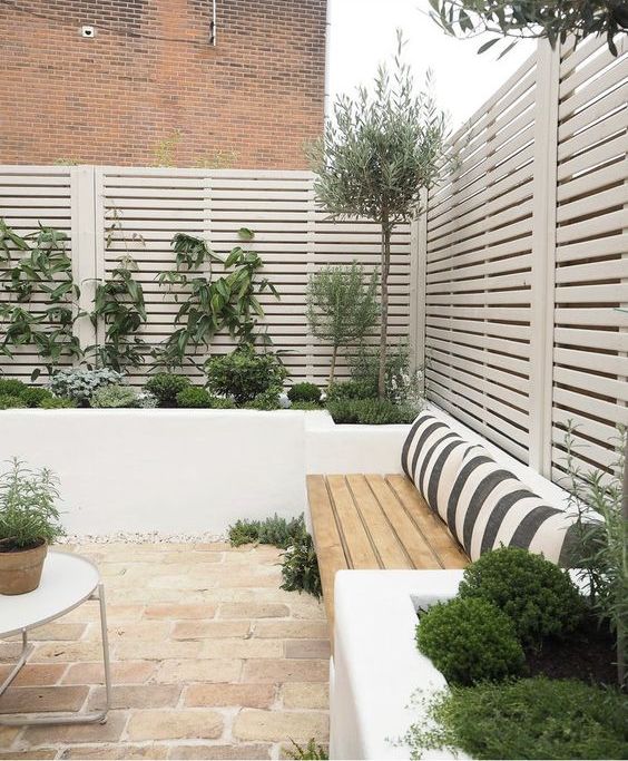 a cool terrace with privacy screens, raised garden beds with greenery, a bench with pillows is a cool space