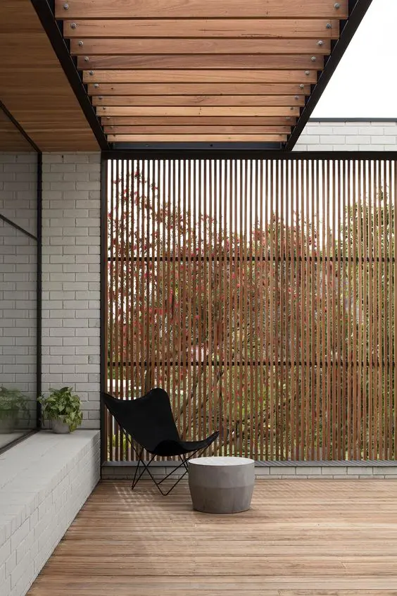 a deck with a stained privacy screen, a black butterfly chair and a side table are a serene and fresh space