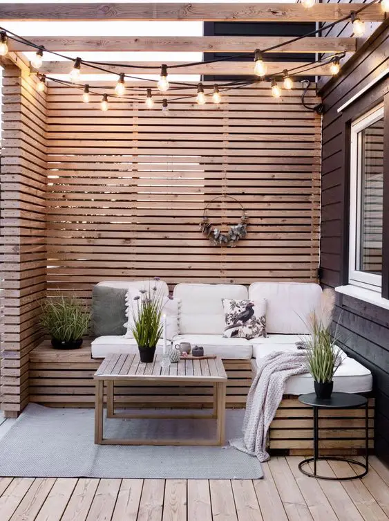 a farmhouse terrace with a stained wooden deck and a corner seat, a stained screen, lights and potted greenery