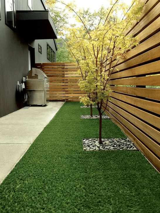 a minimalist side yard with a green lawn, some trees with pebbles and a stained wooden fence for more privacy in the space