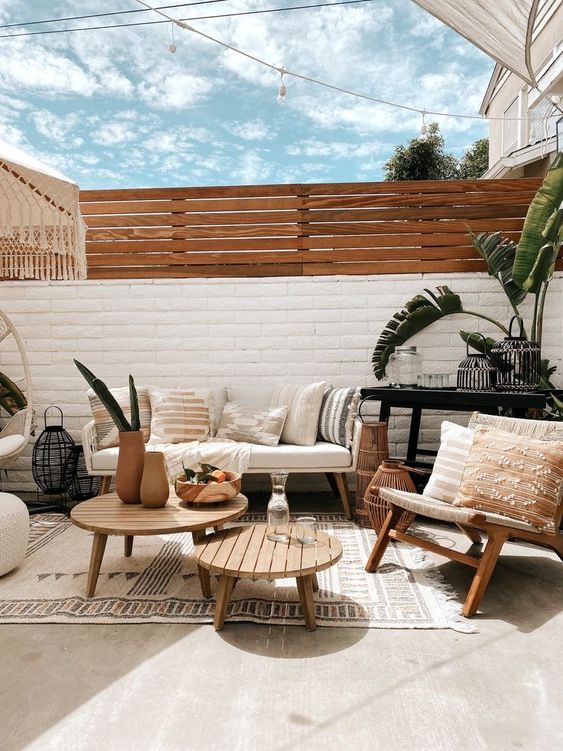 a modern boho terrace with a white fence plus an additional screen, stained furniture, rugs and potted plants