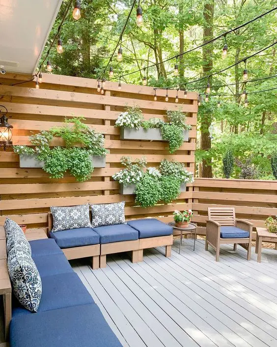 a modern deck with some stained privacy screens, modern sofas and chairs, a coffee table, potted greenery and plants