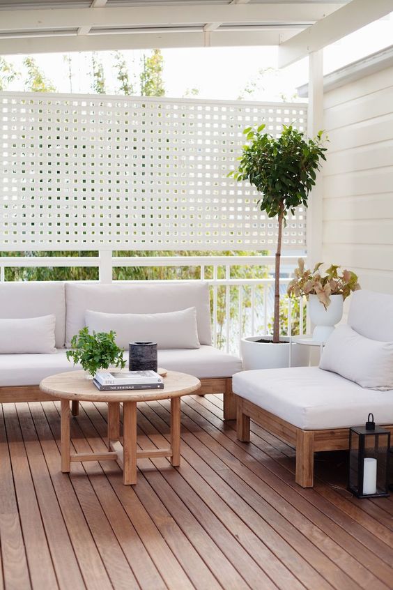 a modern deck with white privacy screens, white outdoor furniture, a coffee table, greenery and a tree