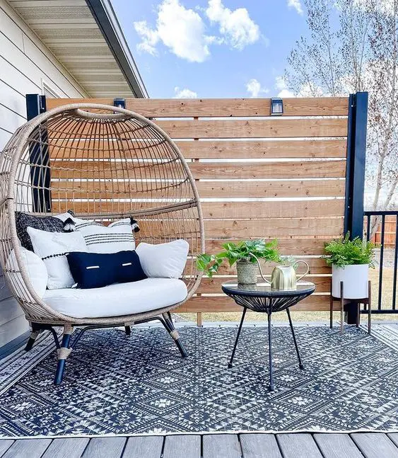 a modern farmhouse terrace with a stained privacy screen, a rattan chair, a side table and some potted plants